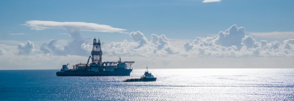 Offshore oil rig with support vessel under a clear sky, highlighting maritime operations