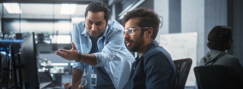 Two professionals collaborating at a computer workstation, one pointing at the screen