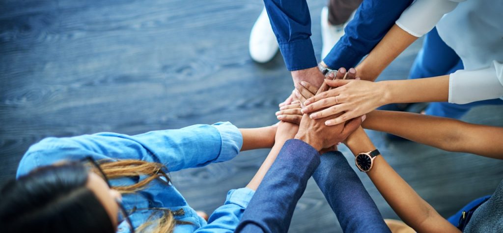 Group of people standing in a circle with hands stacked together, symbolizing teamwork and unity