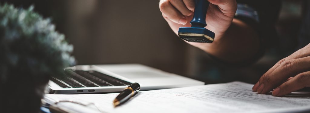 Close‑up of a person stamping official documents next to a laptop, illustrating the verification and approval steps involved in the work permit Guyana process in Guyana.