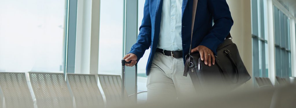 A person walking through an airport terminal holding a suitcase and a work bag, representing international mobility and business travel. They have successfully achieved to receive their work permit guyana